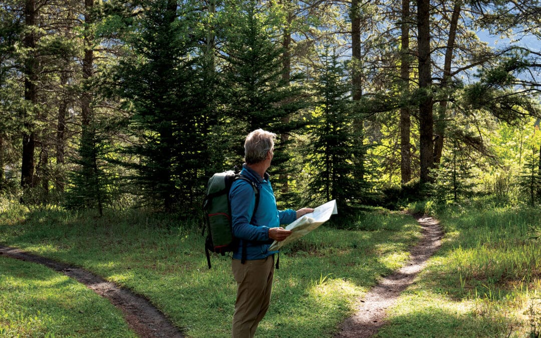 Man hiking in forest looking at map deciding which path to take